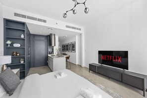 A modern hotel room with a bed, a TV, a kitchenette, and a walk-in closet.