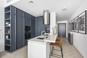 A modern kitchen with grey cabinets, a white island, stainless steel appliances, and a bar stool.