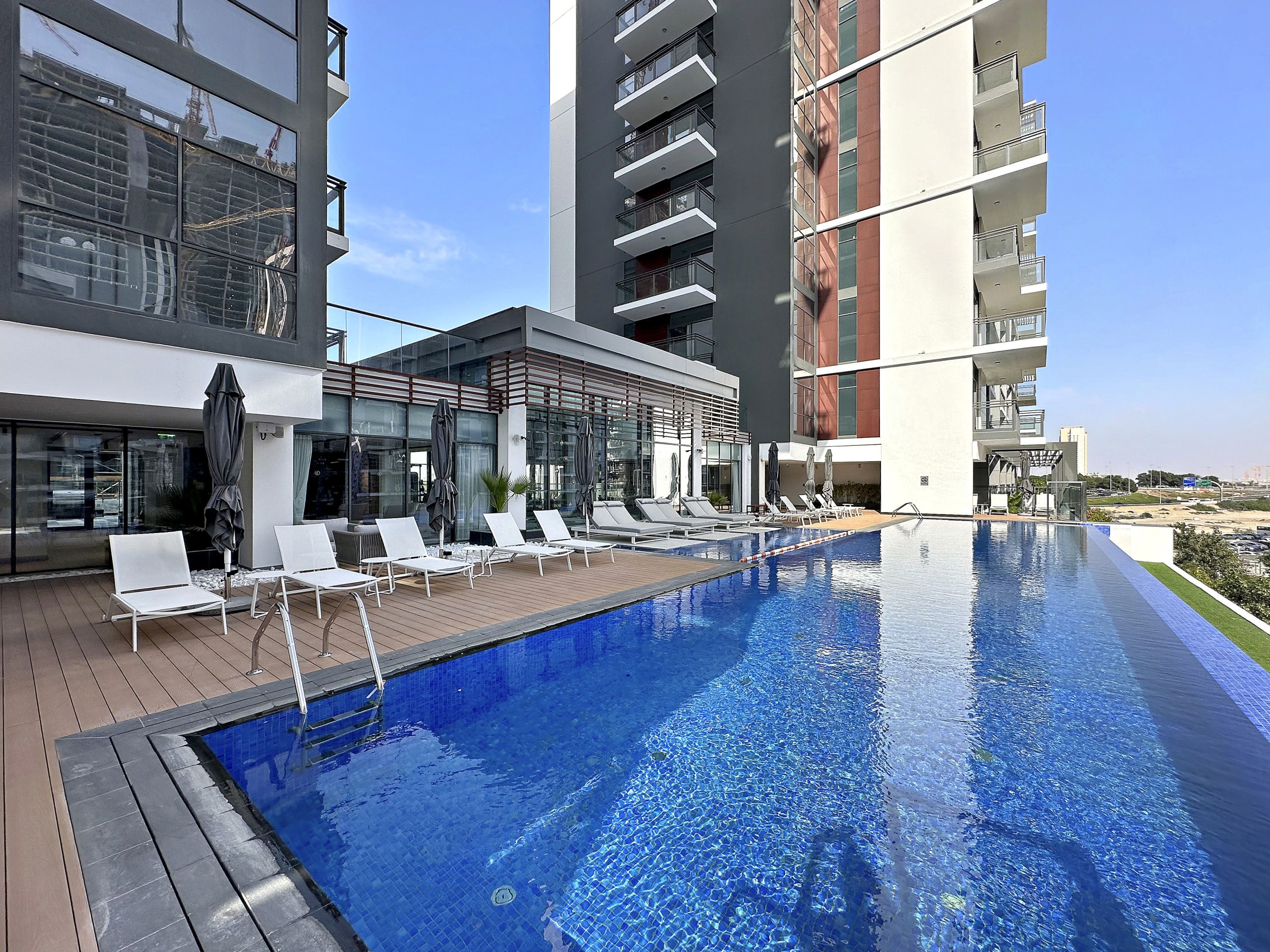A modern hotel with a rooftop infinity pool, lounge chairs, and a glass facade.