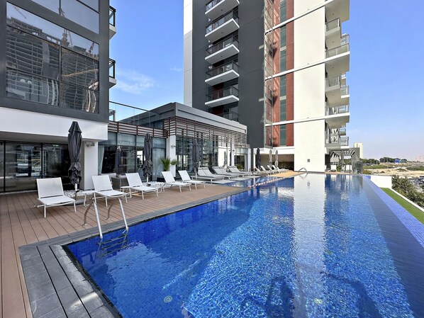 A modern hotel with a rooftop infinity pool, lounge chairs, and a glass facade.