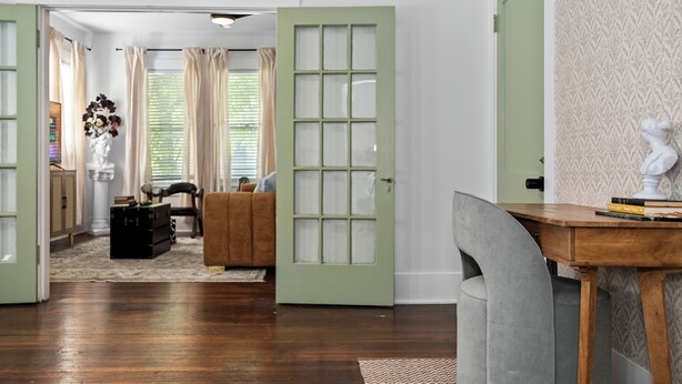 Une pièce avec un plancher en bois, une porte verte, un fauteuil gris, une petite table avec des livres et un buste décoratif accroché au mur.