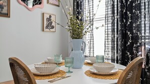 Une table de salle à manger ronde, avec de l’assiette blanche, de la verrerie verte et un vase bleu orné de branches.