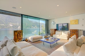 A modern living room with a large window, white sofas, a coffee table, and a flat-screen TV.