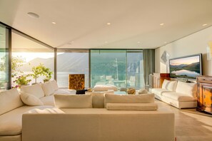 A modern living room with a large sofa, a television, and a view of the sea. - Maison Sur l'Eau (Paradiso)