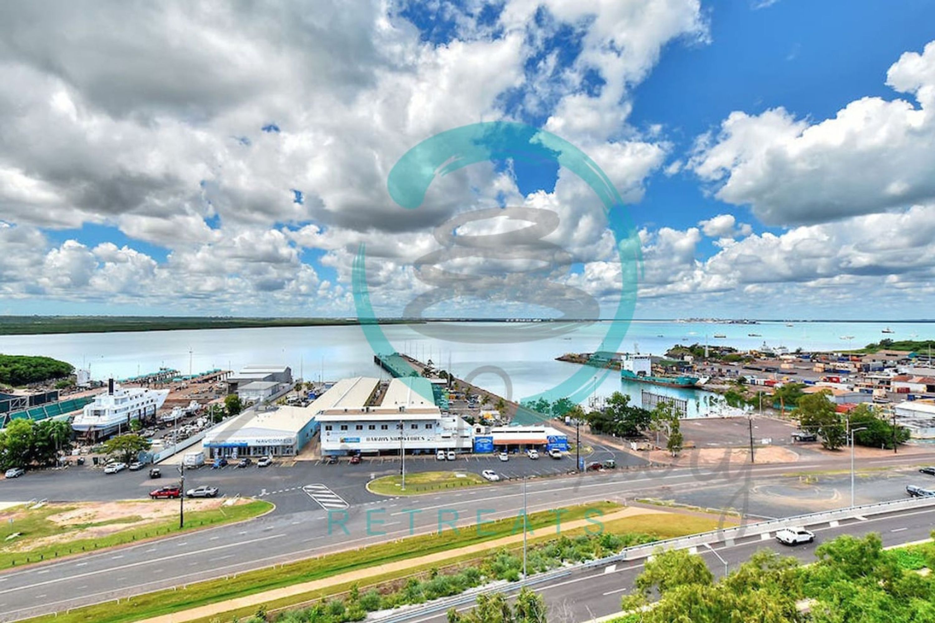 A coastal town with a marina, a large white building with a blue roof, and a road leading to the marina.