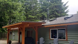 A house with a covered porch, a grill, and three Adirondack chairs. - Timbers by Evergreen Forest Cabins (Ucluelet)