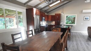 A spacious kitchen with wooden cabinets, a large island, and a dining area with chairs. - Timbers by Evergreen Forest Cabins (Ucluelet)
