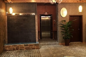 A reception area with a stone wall, an elevator, a potted plant, and a door with a circular light fixture. - Oscar Art Hotel (Jiangyong)