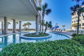 A pool area with palm trees, lounge chairs, and a water slide. - Oceanfront Orange Beach Condo w/ View & Pool! (Orange Beach)