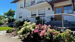 Ein zweistöckiges Gebäude mit einem Balkon, einer Holztür und einer Steintreppe, die zum Eingang führt.