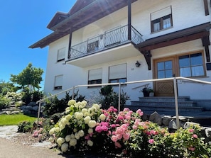 A two-story building with a balcony, a wooden door, and a stone staircase leading to the entrance.