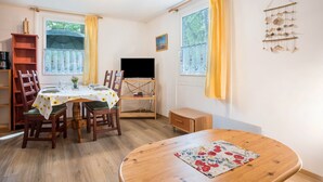 A dining area with a round table, chairs, a television, and a bookshelf.