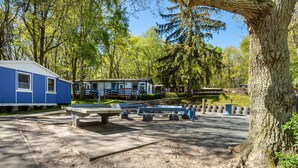 A campsite with a blue cabin, picnic tables, and a large tree.
