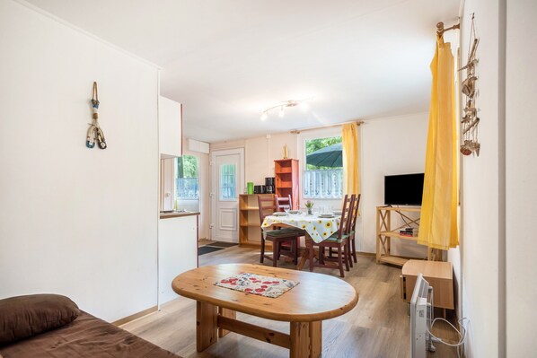 A living room with a wooden table, a sofa, a TV, and a dining area with chairs and a table.