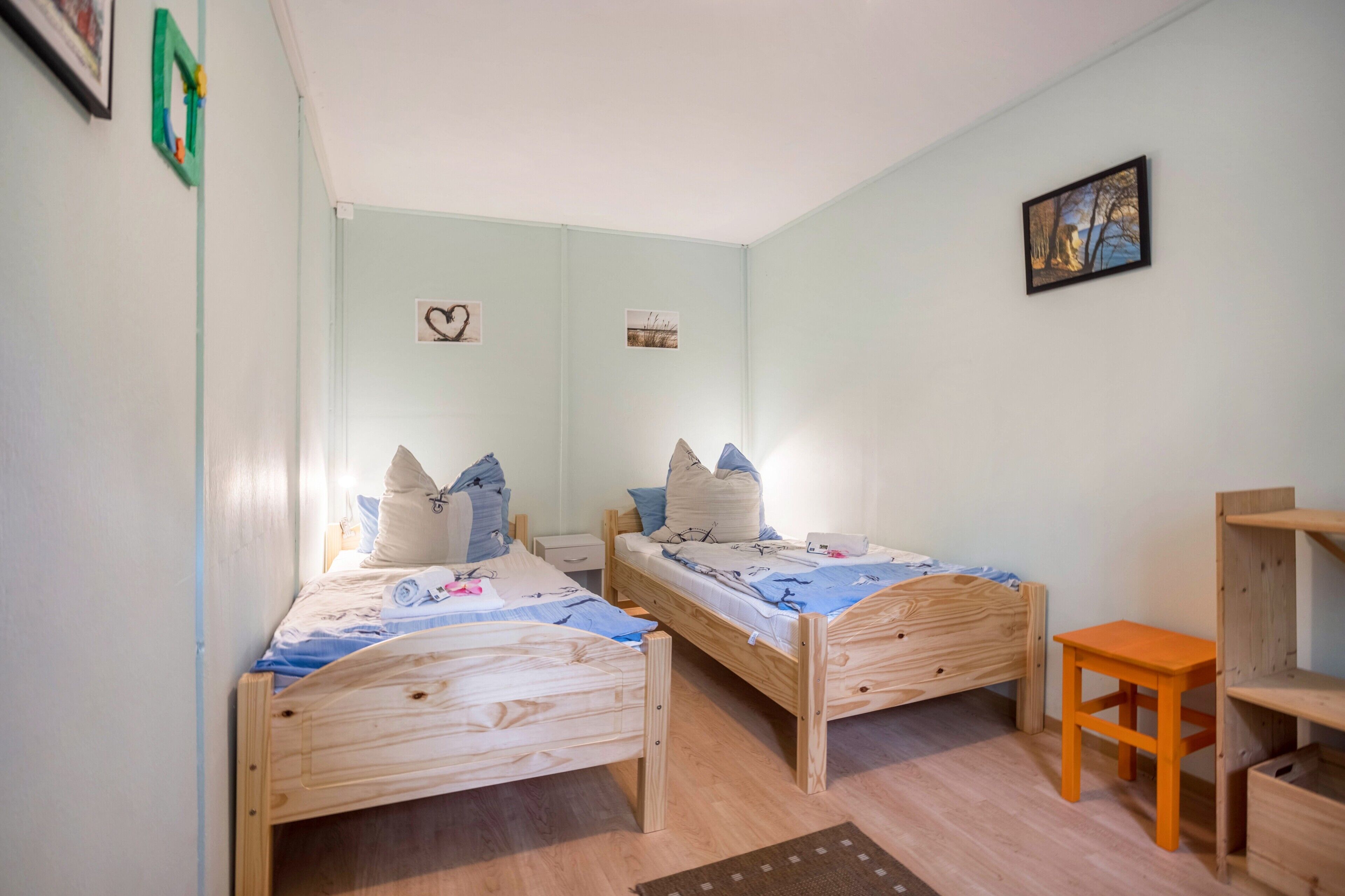 A room with two wooden beds, a small table, and a shelf unit.
