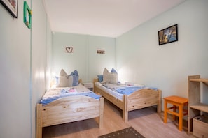 A room with two wooden beds, a small table, and a shelf unit.