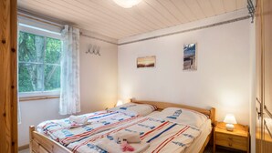 Ein Schlafzimmer mit einem hölzernen Bett, einem Nachttisch mit Lampe, einem Fenster mit Vorhängen und einem Wandbild.