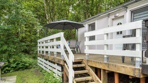 Eine Holzterrasse mit weißer Brüstung führt zu einem Gebäude mit einer Tür und Fenstern.