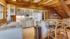 A kitchen with wooden beams, white cabinetry, a stainless steel sink, and a wooden bar area with chairs. - Spacious Rifle Cabin w/ Deck + Mountain Views! (Rifle)