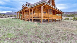 A log cabin with a porch and a chimney, surrounded by a grassy field and mountains. - Spacious Rifle Cabin w/ Deck + Mountain Views! (Rifle)