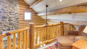 A log cabin interior with a stone wall, wooden beams, a wooden staircase, and a leather sofa. - Spacious Rifle Cabin w/ Deck + Mountain Views! (Rifle)