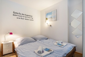Een net opgemaakt bed met een blauw-wit gestreept dekbed, een bedlampje en een muur met een motiverende quote in het Duits.