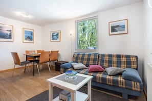 Een woonkamer met een bank, een eettafel, stoelen en lijstwerken aan de muur.