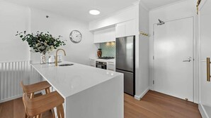 A modern kitchen with white cabinetry, a stainless steel refrigerator, and a central island with bar stools. - Stunning! 2Bed, 1Bath, 1Car, VIEWS ~ CBD (Brisbane City)