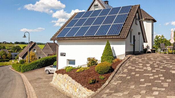 Une maison dotée de panneaux solaires, d’une allée pavée et d’un mur en pierre.