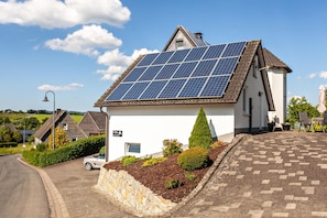 Une maison dotée de panneaux solaires, d’une allée pavée et d’un mur en pierre.