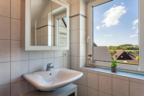 Une salle de bain avec une grande fenêtre, un lavabo et un miroir.