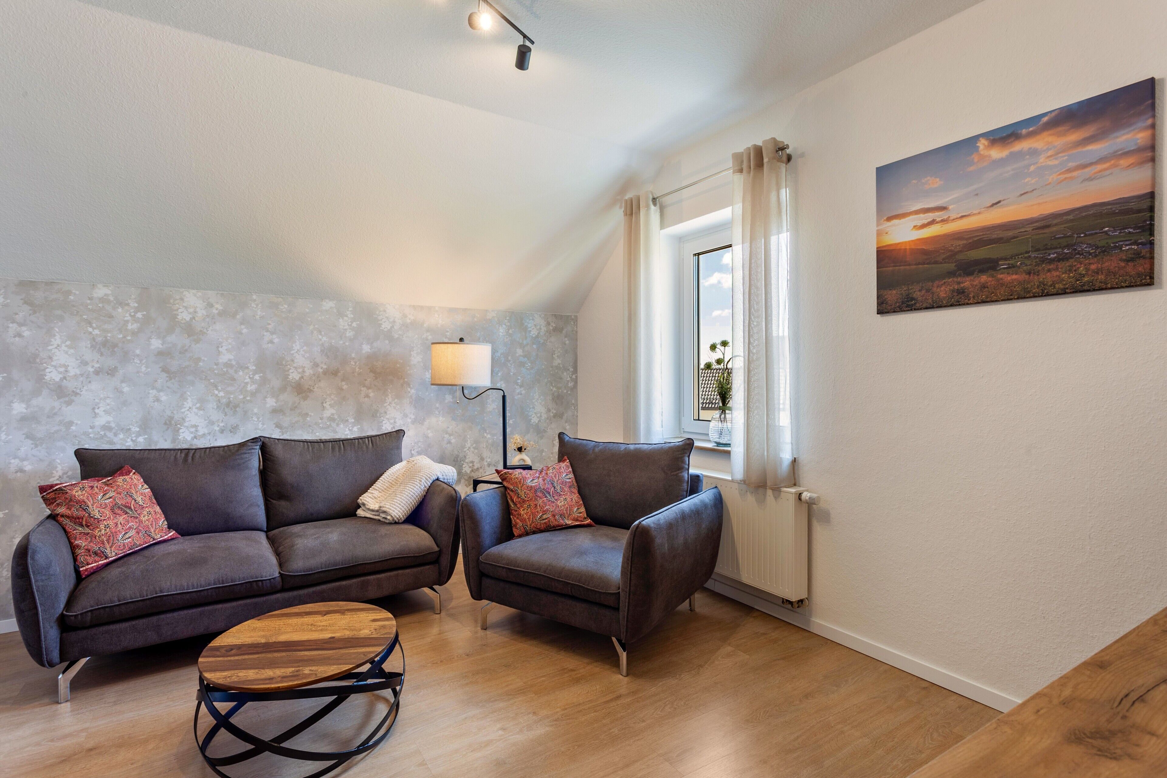 Una sala de estar con sofá, sillón y una mesa de centro, una lámpara y un cuadro en la pared.