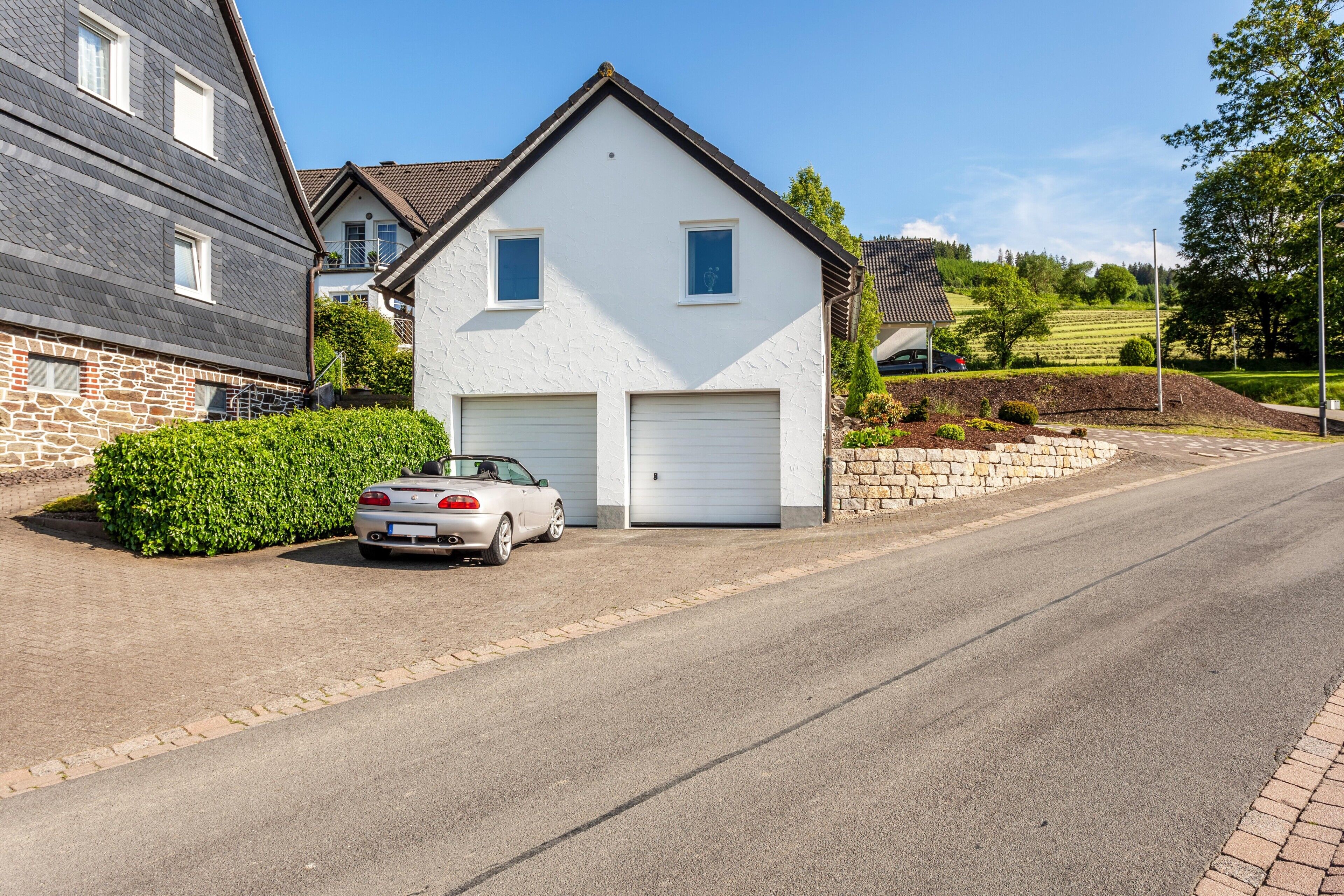 Une maison à deux étages avec un garage, une voiture garée et une pelouse bien entretenue.