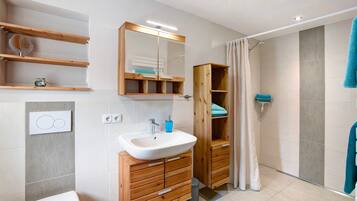 Ein Badezimmer mit einem Holzbadschrank, einem Waschbecken, einem Spiegel, einem Handtuchhalter und einer Duschkabine.