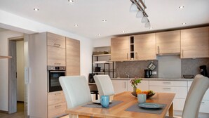 A modern kitchen with built-in appliances, a dining area with a wooden table and chairs, and a walk-in closet. - Apartment 'Ferienwohnung Birke' with Mountain View, Private Terrace and Wi-Fi (Altusried)