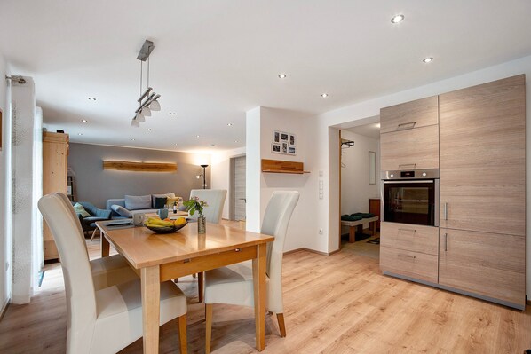 A modern kitchen with wooden cabinets, a built-in oven, and a dining area with a wooden table and chairs.
