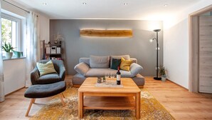 A modern living room with a sofa, armchair, coffee table, and a bookshelf. - Apartment 'Ferienwohnung Birke' with Mountain View, Private Terrace and Wi-Fi (Altusried)