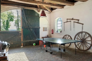 Une table de ping-pong dans une pièce rustique, avec un sol en briques, des poutres en bois et une grande fenêtre.