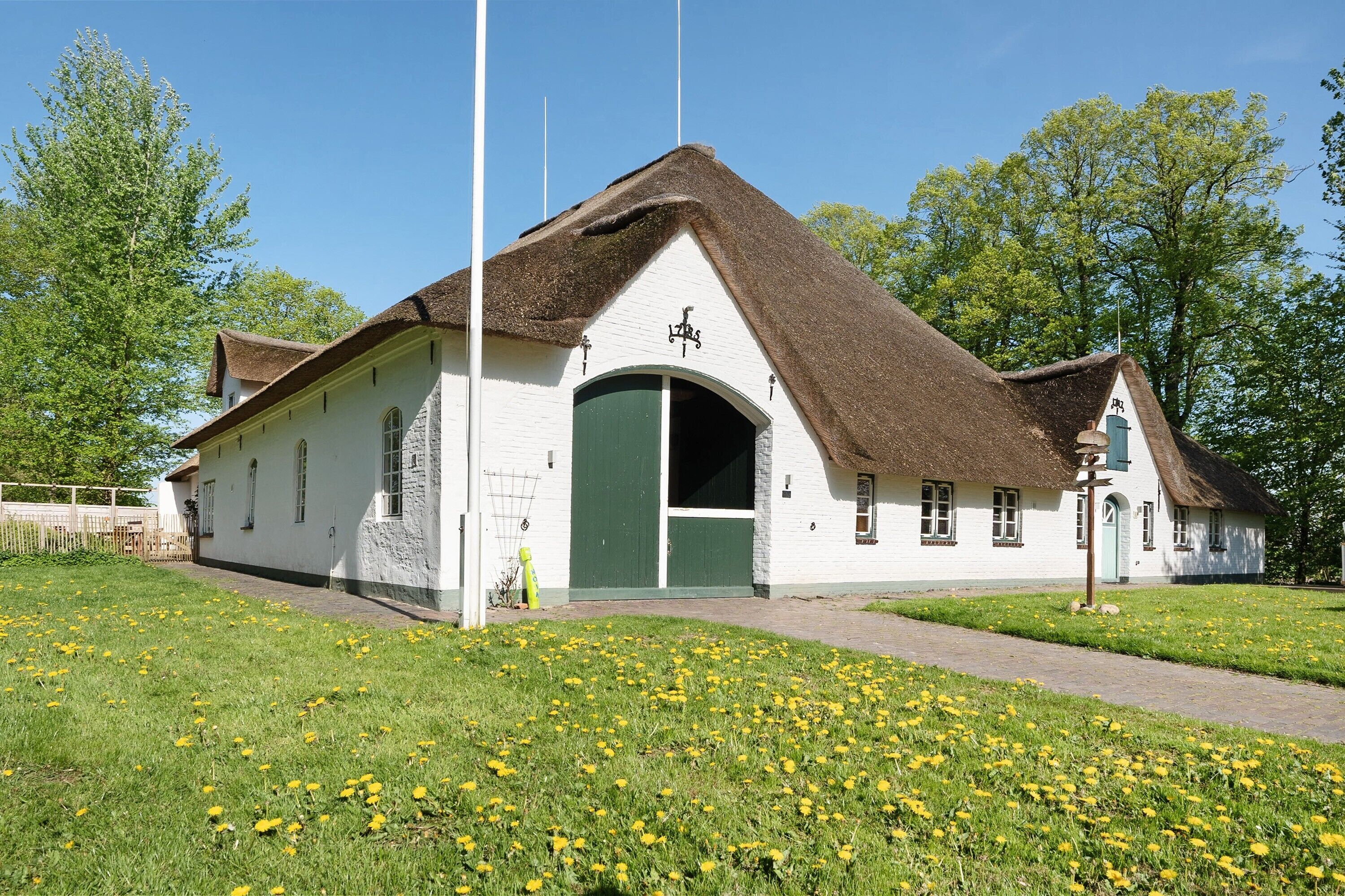 A white building with a thatched roof, a green door, and a flagpole.