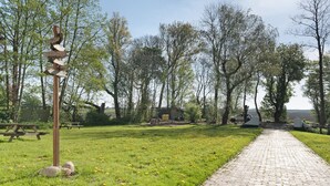 Un sentier pavé mène à un chalet, qui est entouré d’arbres et bordé d’une zone herbeuse parsemée de pissenlits.