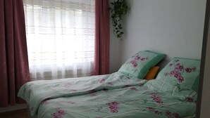 A single bed with floral bedding, a window with sheer curtains, and a hanging plant. - Holiday Apartment 'Gartenland Gela' with Private Terrace, Shared Garden and Wi-Fi (Kitzingen)
