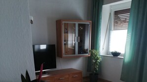 A living room with a wooden floor, a TV, a wooden cabinet, a potted plant, and a window with curtains. - Holiday Apartment 'Gartenland Gela' with Private Terrace, Shared Garden and Wi-Fi (Kitzingen)