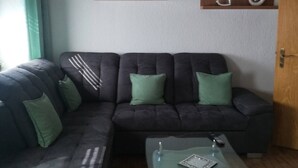 A living room with a dark-colored sofa, a glass coffee table, and two wall-mounted shelves with decorative items. - Holiday Apartment 'Gartenland Gela' with Private Terrace, Shared Garden and Wi-Fi (Kitzingen)