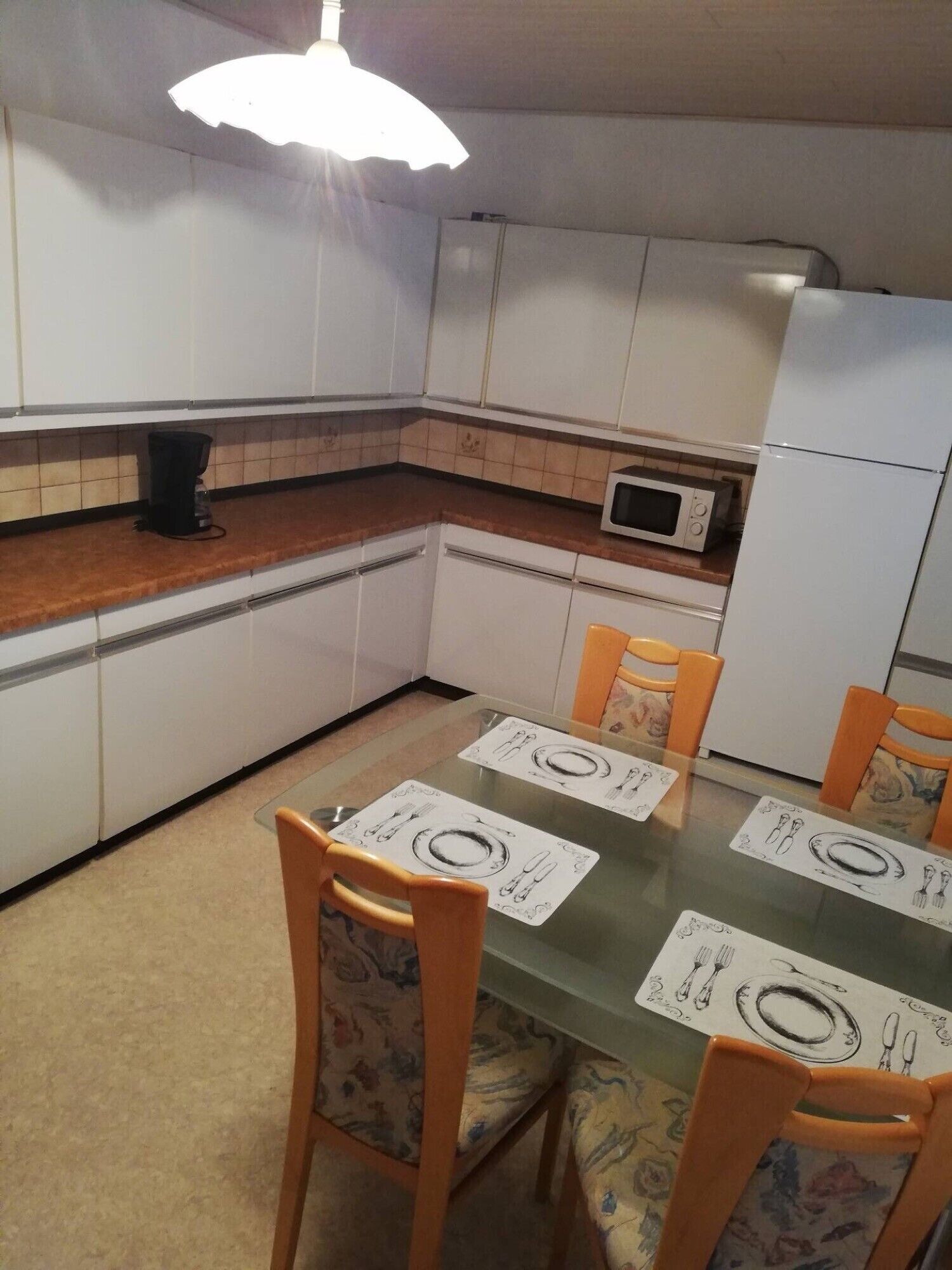 Una cocina con gabinetes blancos, microondas, refrigerador y una mesa de comedor con sillas.