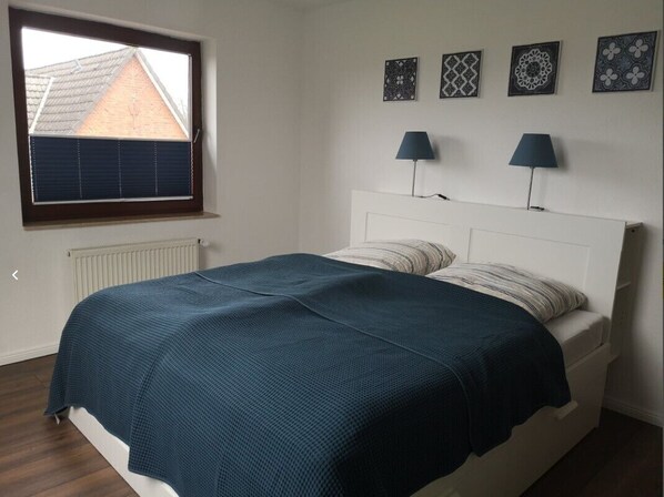 A bedroom with a bed, a window with blinds, a radiator, and wall-mounted lamps.