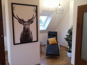 A room with a framed deer artwork, a reclining chair with a cushion, a potted plant, and a skylight.