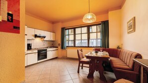A kitchen with a dining area, a large window with curtains, and a hanging light fixture. - Apartment 'Eulennest 1' with Private Terrace and Wi-Fi (Minheim)