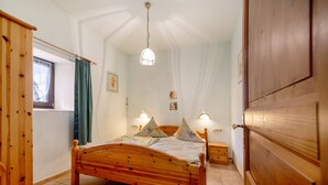 A wooden bed with a headboard, two bedside tables, a hanging light fixture, and a window with curtains. - Apartment 'Eulennest 1' with Private Terrace and Wi-Fi (Minheim)