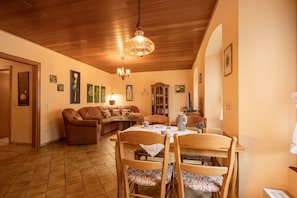 Un coin repas avec une table et des chaises en bois, un lustre et un canapé en arrière-plan.