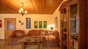 A living room with a wooden ceiling, a glass-top coffee table, brown leather sofas, a wooden cabinet with glass doors, and wall art.